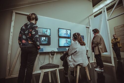 Menschen mit Kopfhörern vor Bildschirmen - Anschauen des Videomaterials der Ausstellung